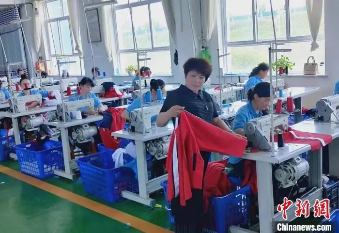 圖為臨夏縣翠夢飛服裝加工有限責(zé)任公司總經(jīng)理唐小翠(中)在制衣工廠內(nèi)檢查衣服質(zhì)量